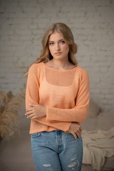 a woman standing in front of a brick wall wearing ripped jeans and an orange sweater