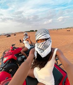 two women riding on the back of a red four - wheeler in the sand dunes