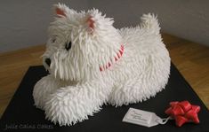 a cake shaped like a white dog laying on top of a wooden table next to a red bow