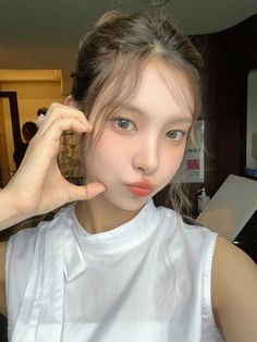 a young woman poses with her hand on her head and looking at the camera while wearing a white shirt