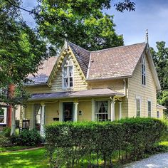 a yellow house with a red door and white trim on the front, surrounded by green bushes