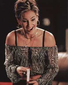 a woman laughing while holding a cell phone in her right hand and wearing an animal print top