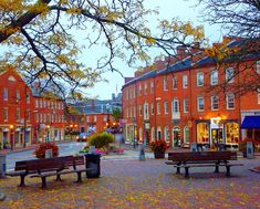 an empty street with benches and tables in front of red brick buildings on either side