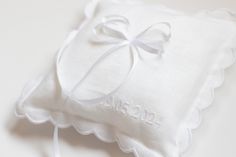 a small white pillow with a bow on the side and name embroidered on the front