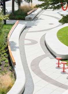 an empty park with benches and trees on the side walk, surrounded by greenery