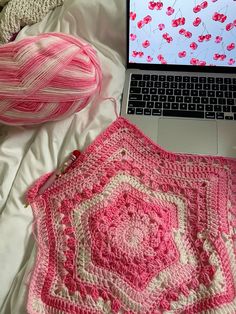 a laptop computer sitting on top of a bed next to a pink crocheted blanket