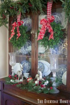 a china cabinet decorated with christmas wreaths and greenery