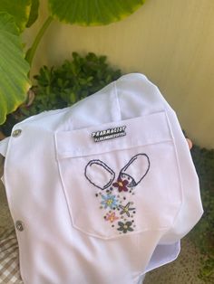 a close up of a person's hand holding a white shirt with flowers on it