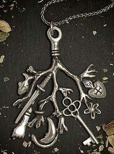 a silver necklace with various items attached to it on a black surface, including scissors and spoons