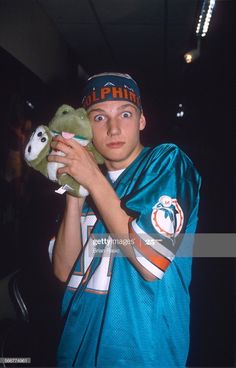 a young man holding a stuffed animal in his hands and looking at the camera while wearing a football uniform