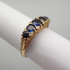 Vintage English 18k (.750) yellow gold ring, featuring ornate setting with 5 Sapphire stones and tiny Diamond accents. Maker's mark - J&P (unknown). This majestic ring is a size 6 1/4, it is 5.36 mm wide, weighing 4.4 grams. EA5543 Formal Yellow Gold Three Stone Rings, Antique Yellow Gold Sapphire Ring With Round Cut, Elegant Three Stone Sapphire Ring In Yellow Gold, Elegant Three Stone Yellow Gold Sapphire Ring, Victorian Multi-stone Yellow Gold Rings, Classic Multi-stone Sapphire Ring, Classic Gold Multi-stone Sapphire Ring, Victorian Gold Three-stone Ring, Victorian Gold Three Stone Ring