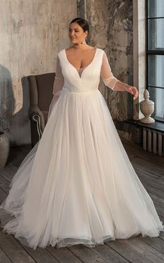 a woman in a white wedding dress standing on a wooden floor next to a chair