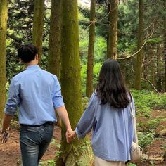 a man and woman holding hands walking in the woods with trees on either side of them