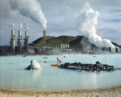 some people are in the water and steam is coming out of the stacks behind them