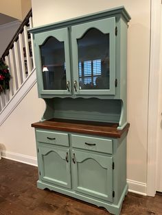 a blue china cabinet sitting in the corner of a room next to a stair case