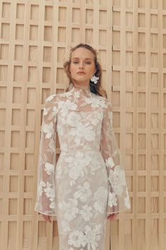 a woman standing in front of a wooden wall wearing a white dress with flowers on it