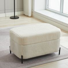 a white ottoman sitting on top of a rug in a living room next to a window