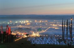 a large field filled with lots of tents and lights at night in the distance is a city