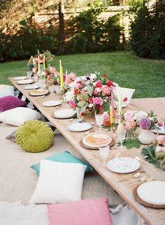 a long table with plates and flowers on it in the middle of a grassy area