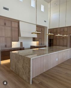 a large kitchen with wooden cabinets and marble counter tops, along with two pendant lights hanging from the ceiling