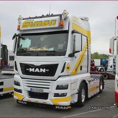 a white and yellow semi truck parked in a parking lot next to other trucks on the road