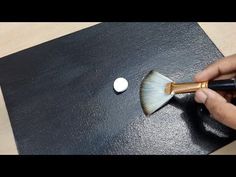 someone using a brush to paint the top of a black piece of leather with gold trim