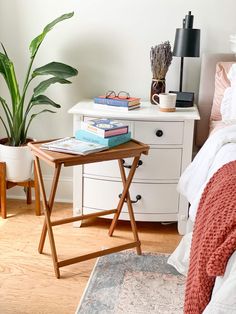 a bed room with a neatly made bed next to a nightstand and a potted plant