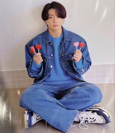 a person sitting on the ground with some lollipops in their hands and holding two hearts