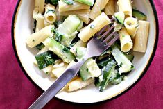 a white bowl filled with pasta and spinach on top of a pink table cloth