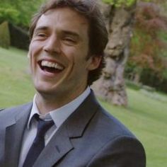 a man in a suit and tie smiling at the camera with trees in the background