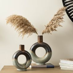 two vases with plants in them sitting on a table next to books and a clock