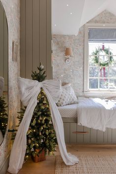 a small christmas tree in the corner of a room next to a bed and window