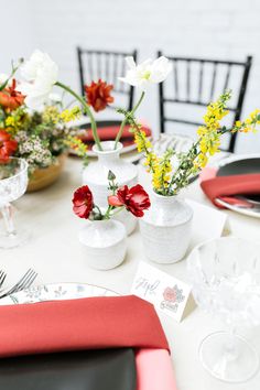 the table is set with red and white flowers in vases, place cards, and silverware