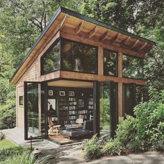 a small house with lots of windows and bookshelves on the outside, surrounded by greenery