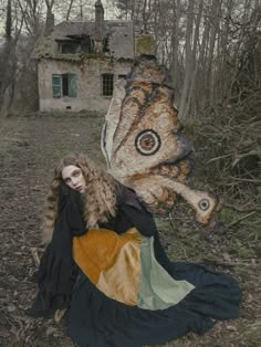 a woman sitting on the ground in front of a butterfly statue with a house behind her