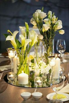 a table with candles and flowers in vases on top of it, surrounded by other place settings