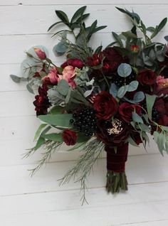 a bouquet of red flowers and greenery on a white wooden surface with wood planks