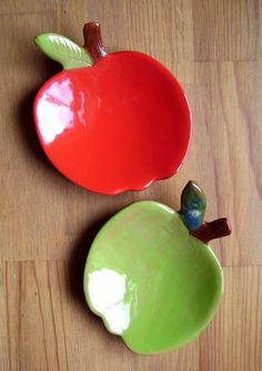 two apple shaped dishes sitting on top of a wooden table next to each other, one green and the other red