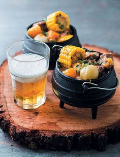 a wooden table topped with a bowl of food next to a glass filled with beer