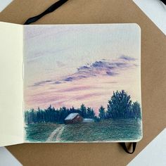 an open notebook with a drawing of a road and trees in the background at sunset