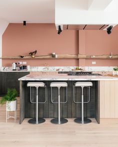 three stools sit at the center of a kitchen island with marble countertops and pink walls