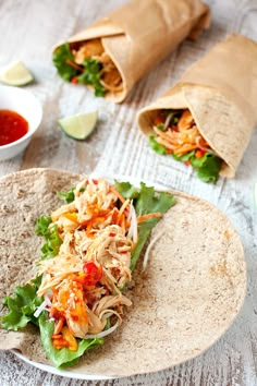 a tortilla filled with shredded chicken and lettuce next to dipping sauce