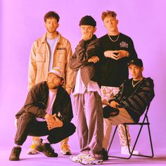 four young men posing for a photo in front of a purple background with one sitting on a chair and the other standing