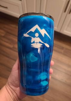 a person is holding up a blue cup with a white house on it in the middle of a kitchen