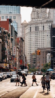 several people crossing the street in front of tall buildings and traffic lights on a busy city street