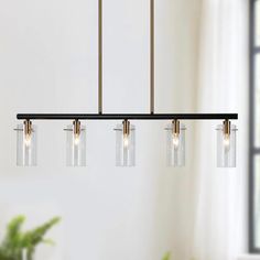 three lights hanging over a dining table in a room with a potted plant on the side