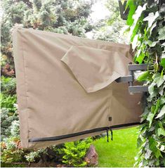 an outdoor grill cover hanging from the side of a tree in front of some bushes