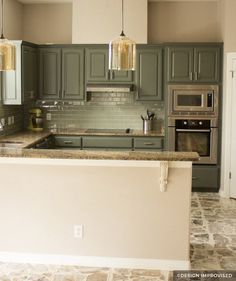 a kitchen with green cabinets and marble counter tops, an oven in the corner and two pendant lights hanging from the ceiling