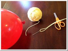 a ball of yarn, scissors and balloon sitting on a wooden table next to each other