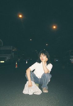 a woman sitting on the ground with her hand under her chin and looking at the camera